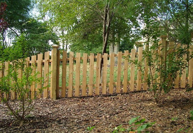 A wooden picket fence is surrounded by trees and leaves.