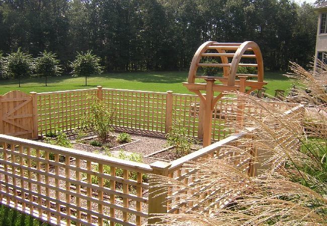 A wooden fence surrounds a garden with trees in the background