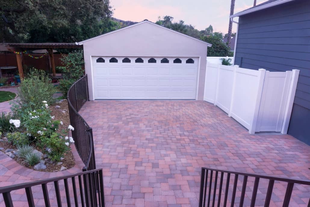 A brick driveway with a white garage door and a white fence