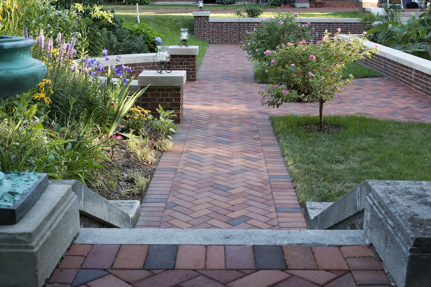 A brick walkway leading to a lush green garden