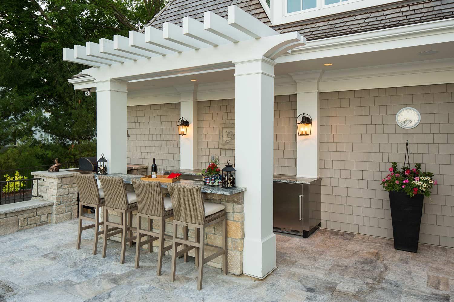 A patio with a pergola , a table and chairs underneath it.