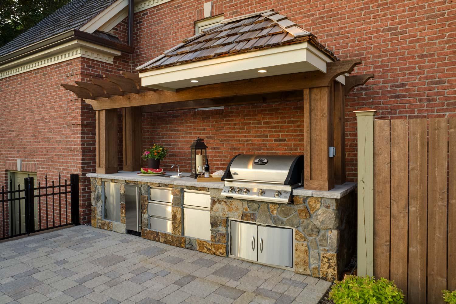 A large outdoor kitchen with a grill and a wooden pergola.