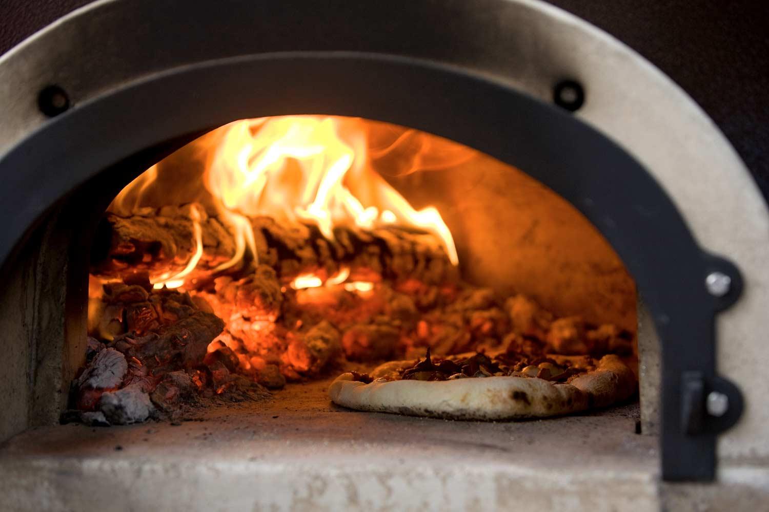 A pizza is being cooked in a wood fired oven.