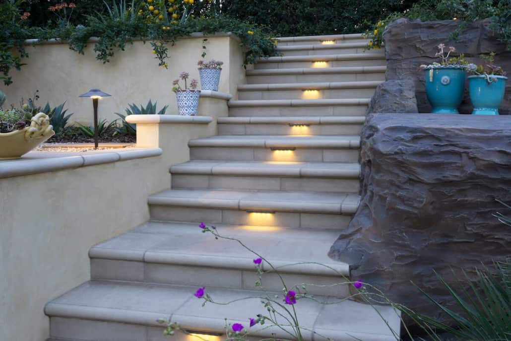 A set of stairs with lights on them leading up to a rock wall.