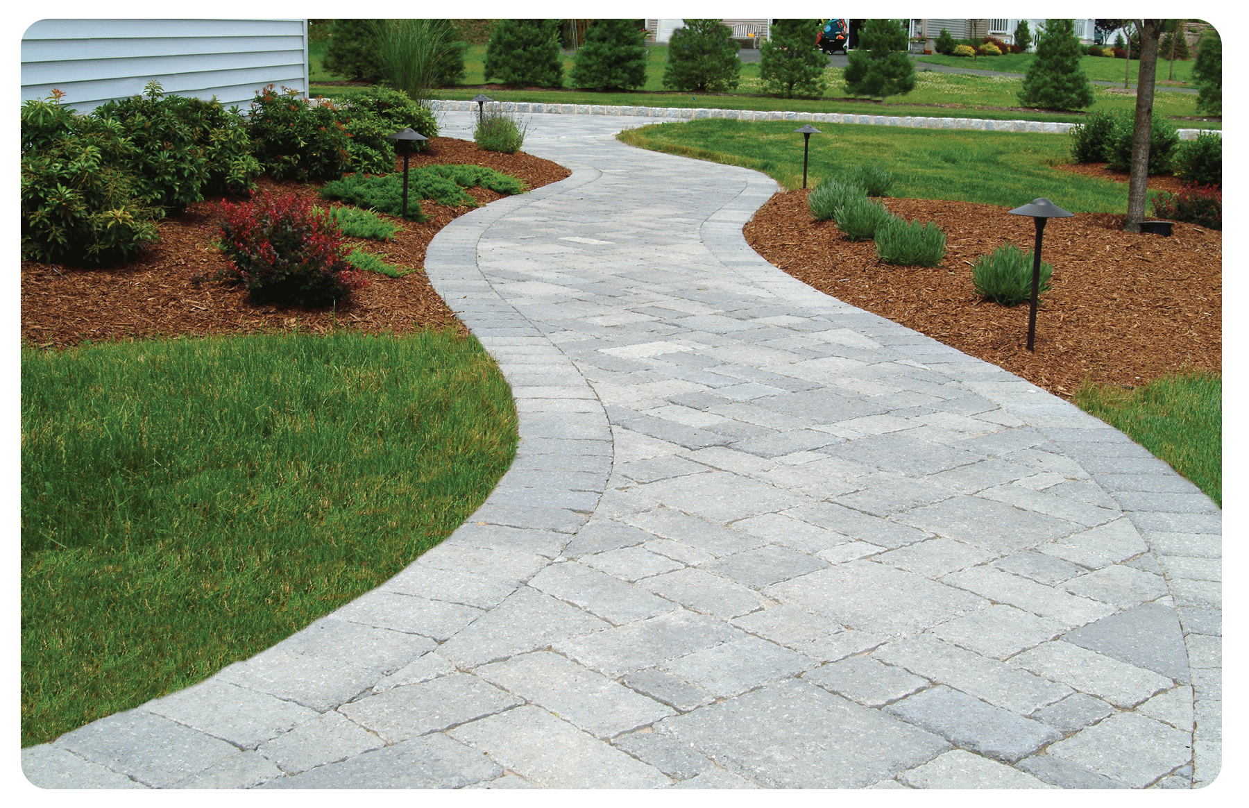 A brick walkway going through a lush green yard