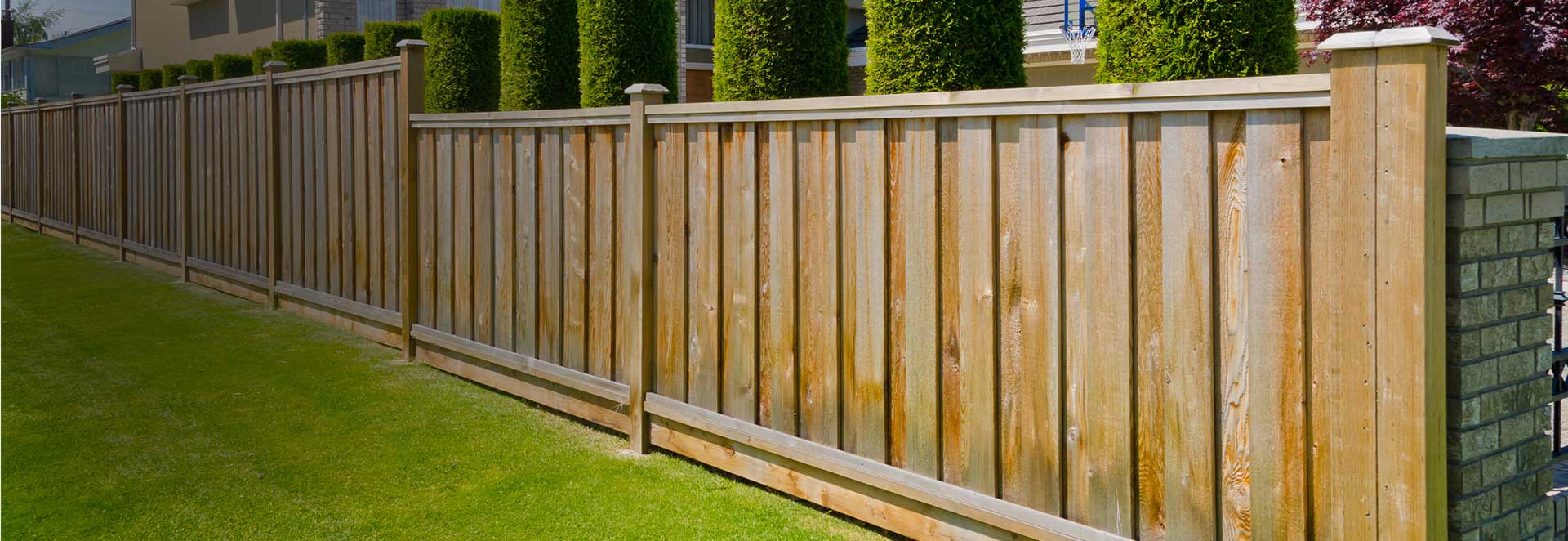A wooden fence surrounds a lush green lawn in front of a house.