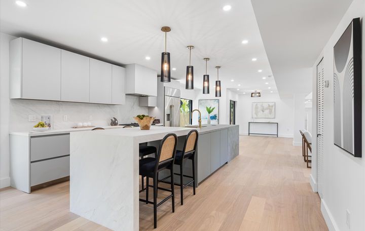 A kitchen with white cabinets , a large island , and stools.