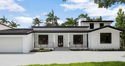 A white house with a black roof is surrounded by palm trees.