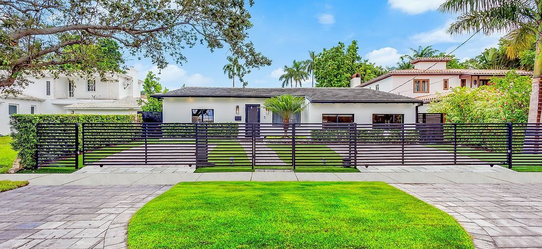 A white house with a black fence and a large lawn in front of it.