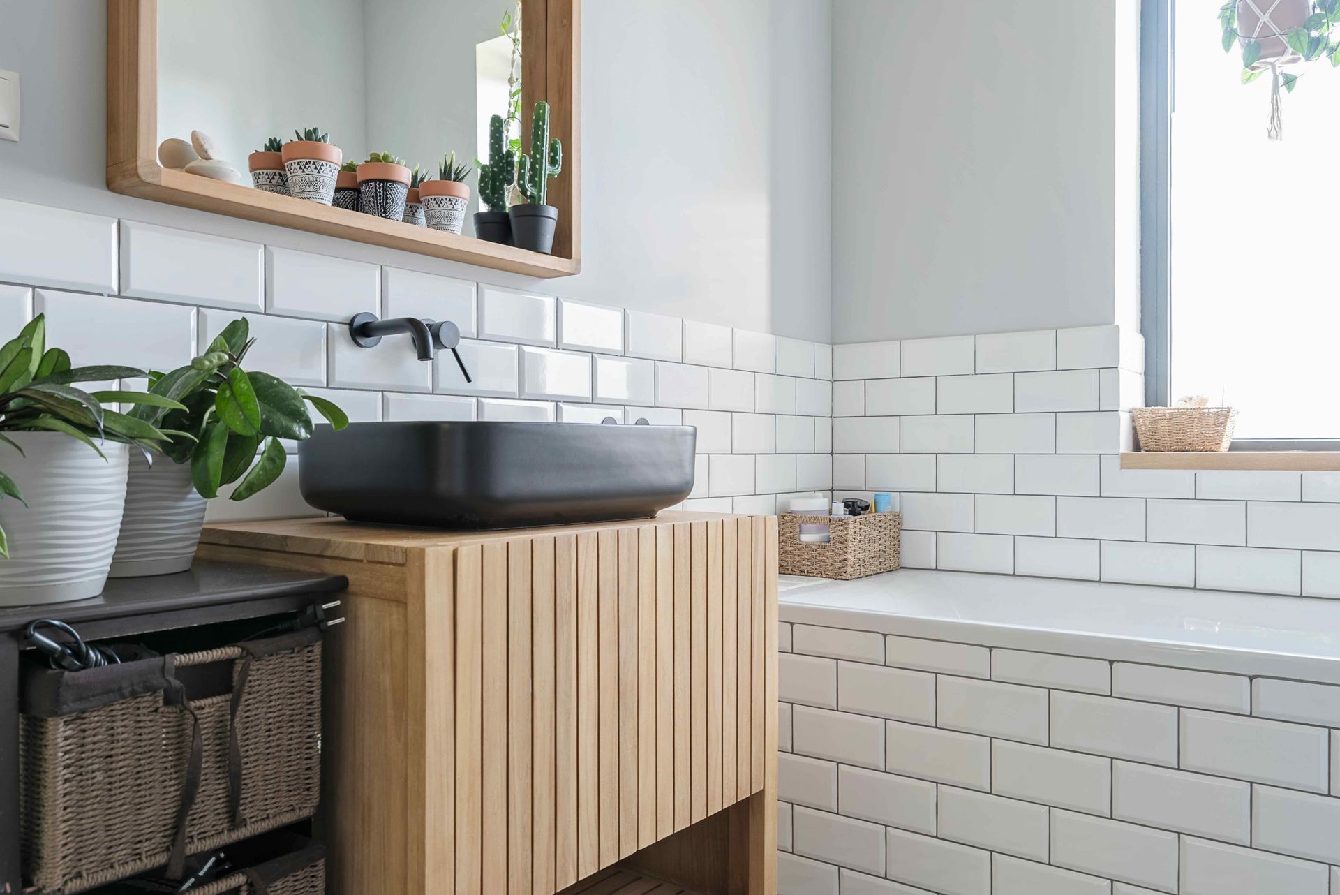 A bathroom with a black sink, white tile, a mirror and a bath tub