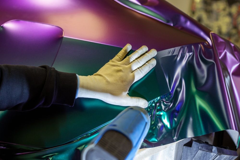 A person is wrapping a car in purple and green foil.