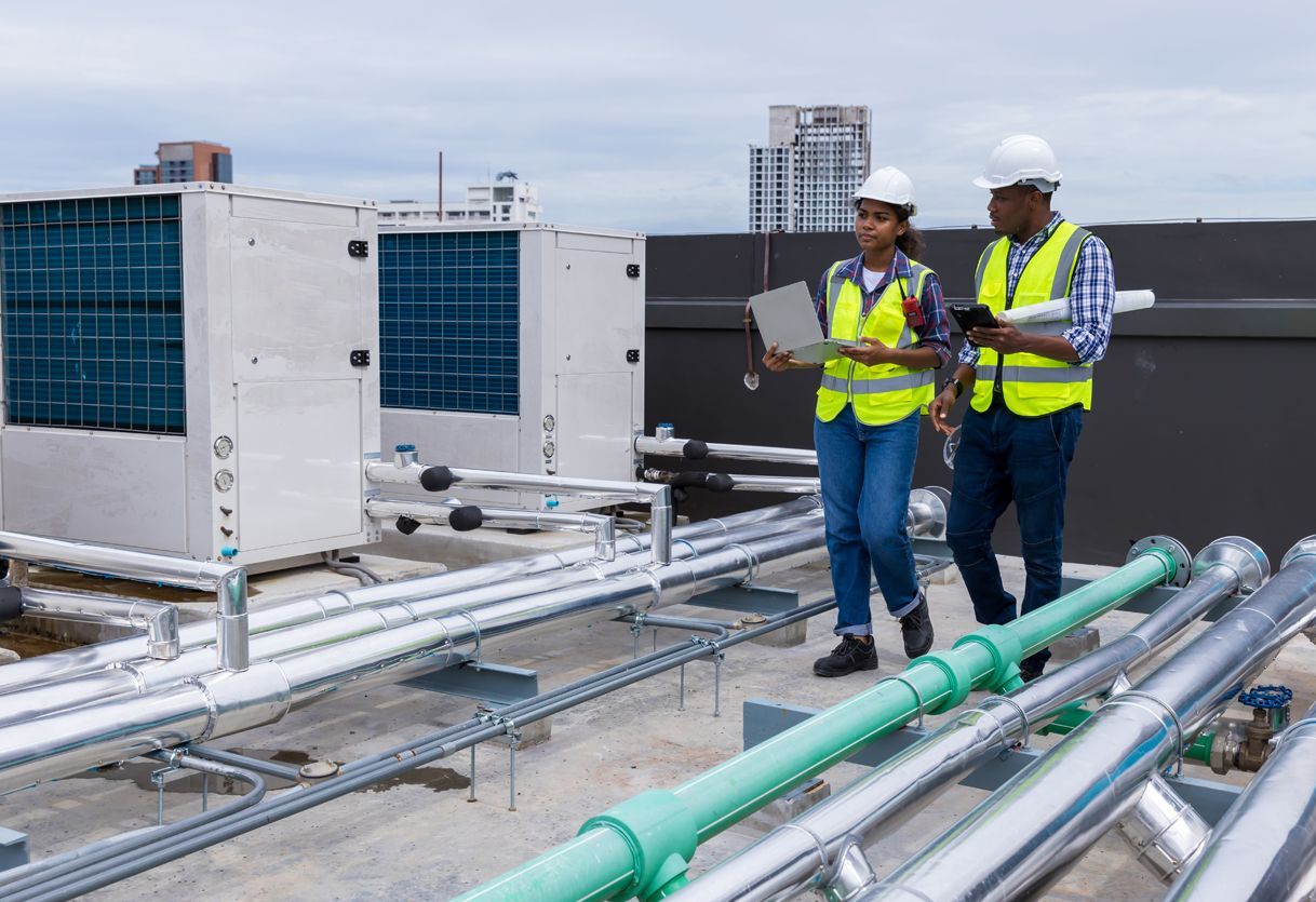 A man and a woman are standing on top of a roof looking at a laptop.