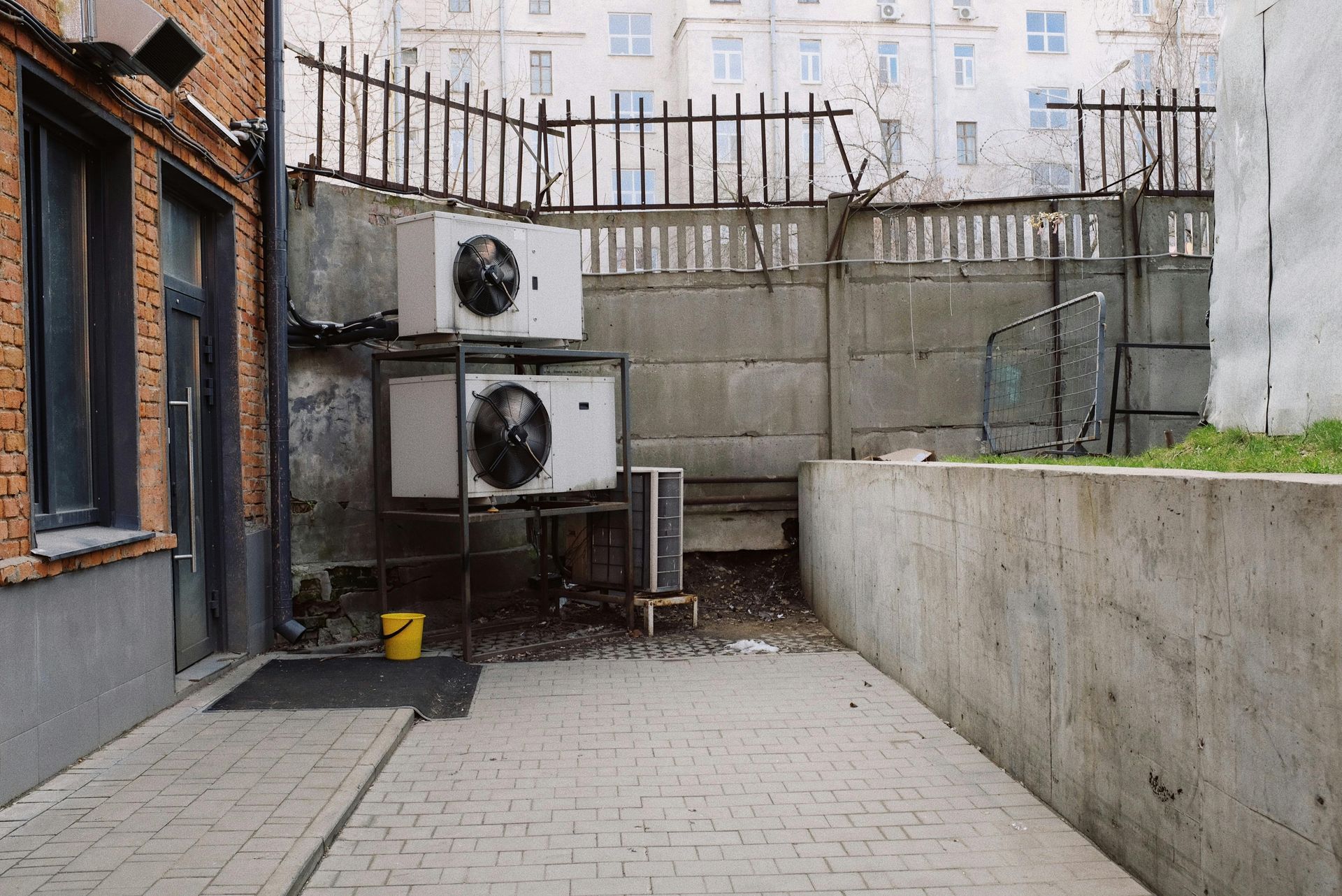 Back alley with brick building, concrete walls, air conditioning units, and a fence.