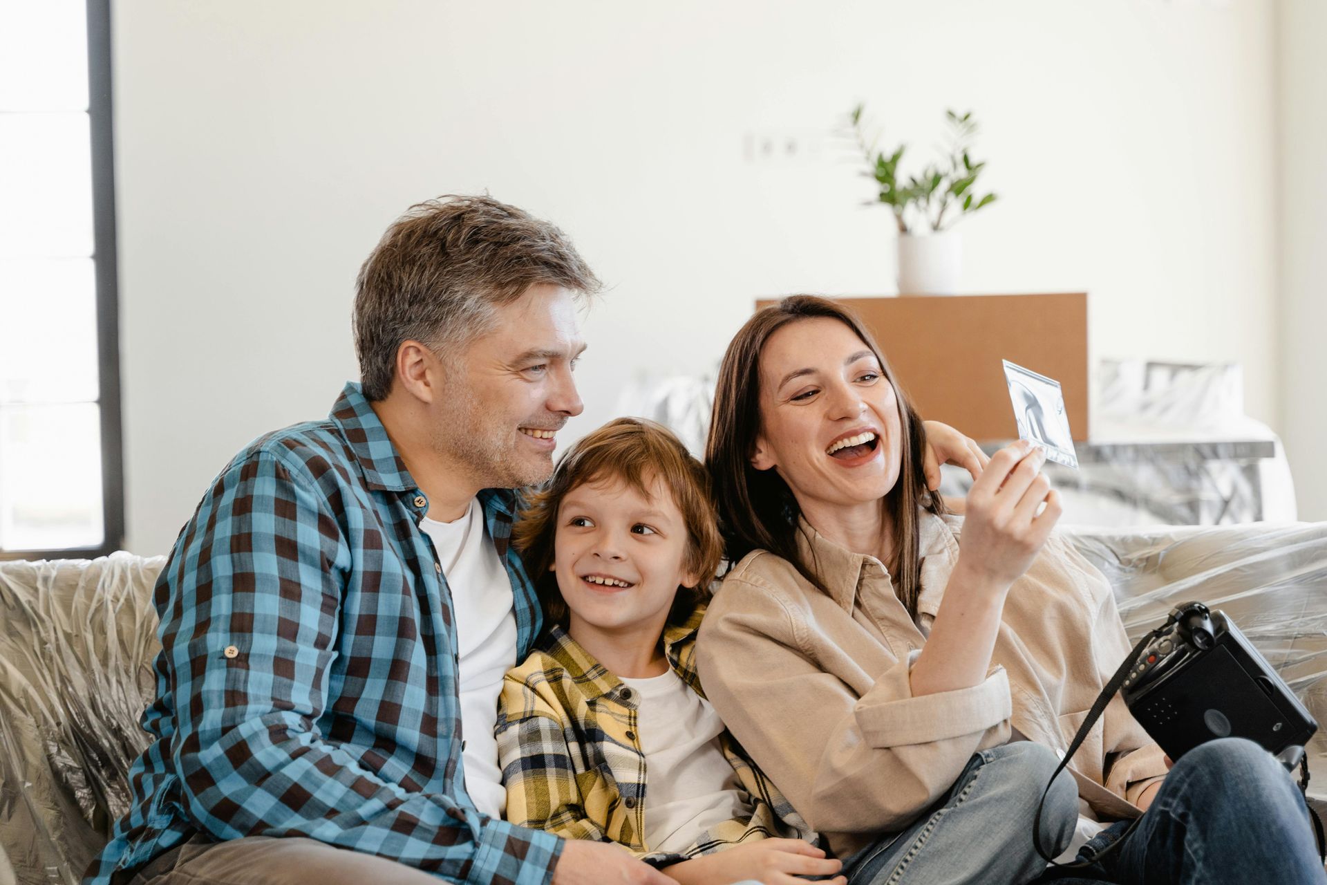 Family of three laughing together in a new home, looking at a photo.