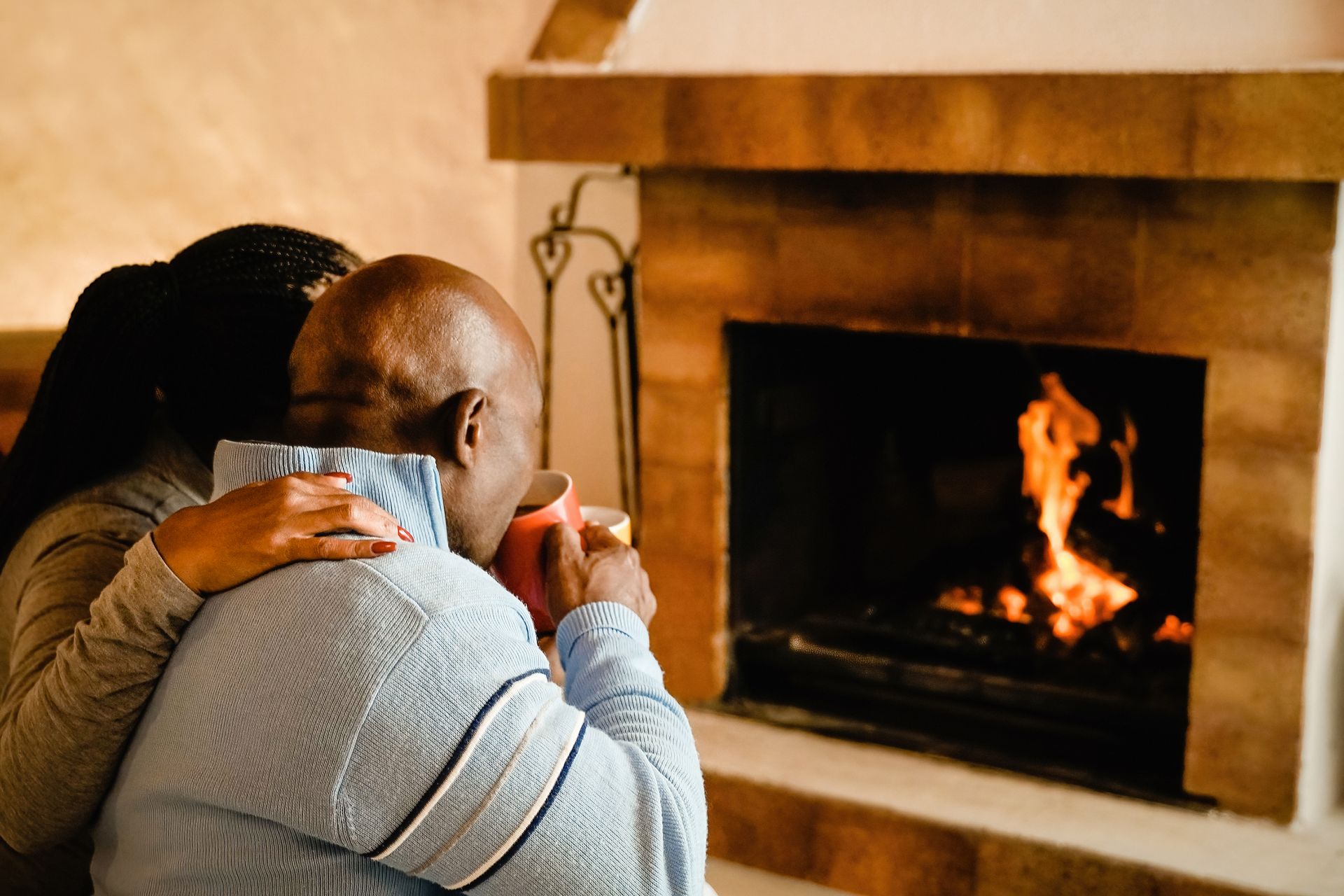 Family sits on the floor around a wood-burning stove in a cozy room.