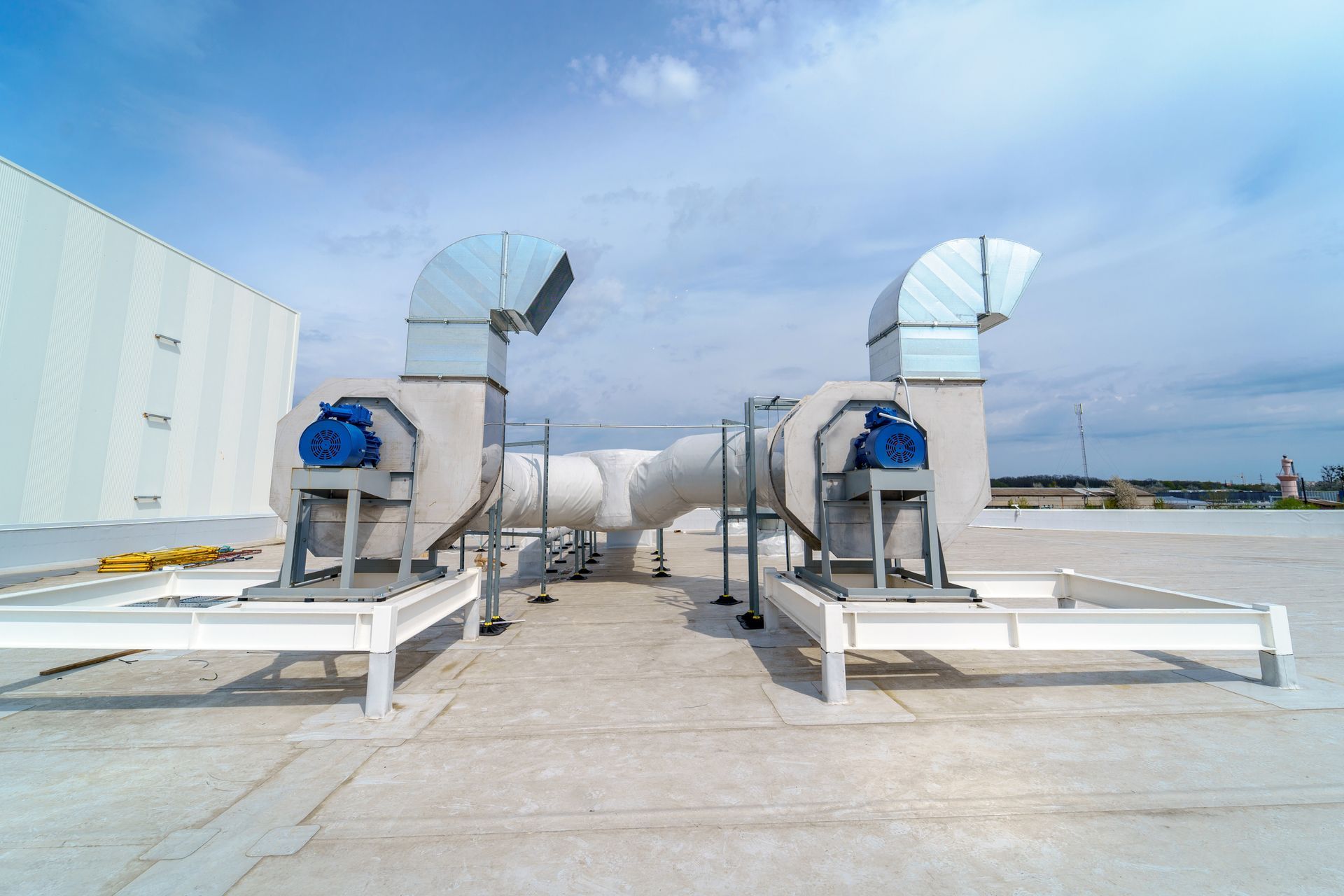 Two rooftop HVAC units with silver ductwork and blue motors against a blue sky.