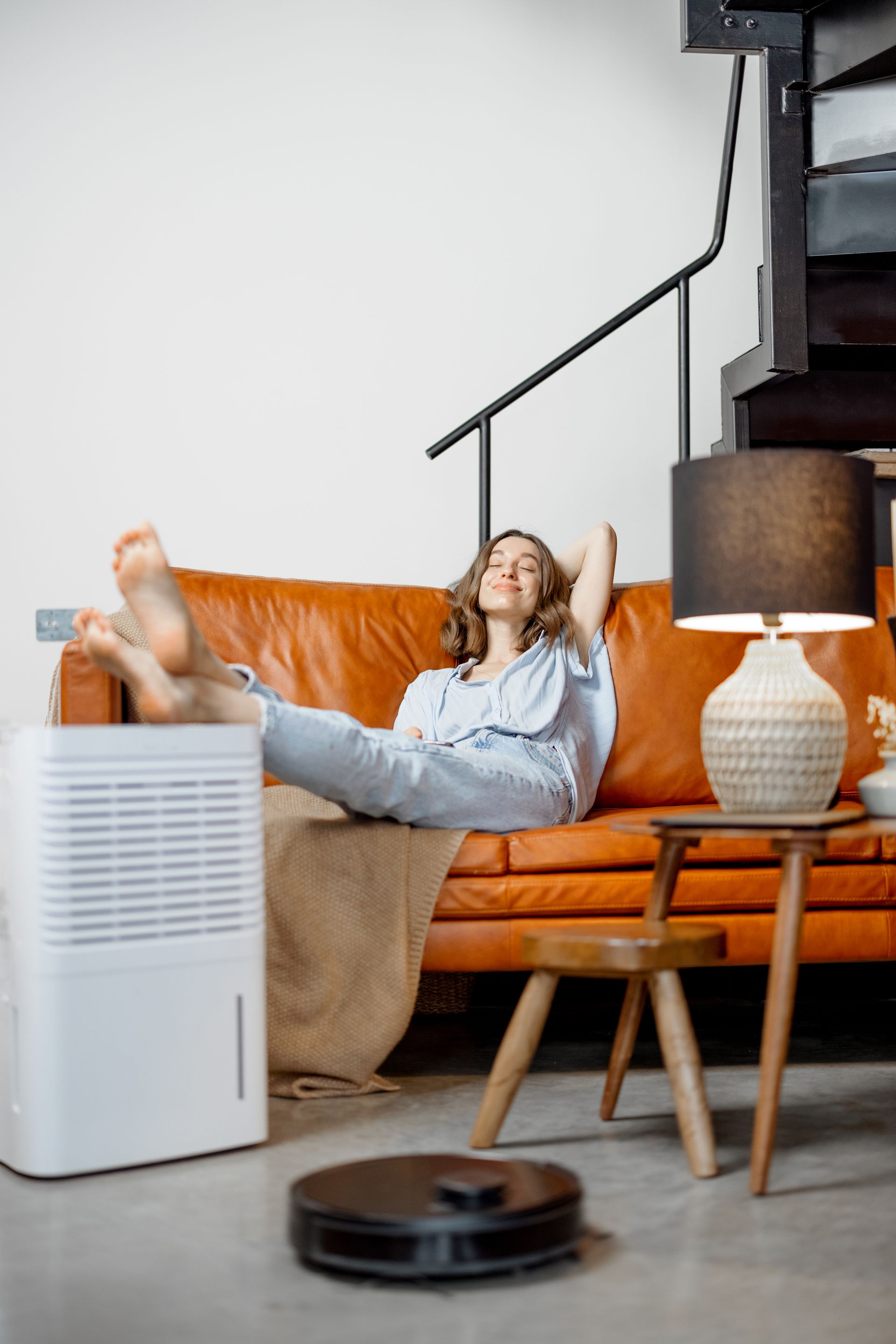 A woman is sitting on a couch in a living room next to a air conditioner.