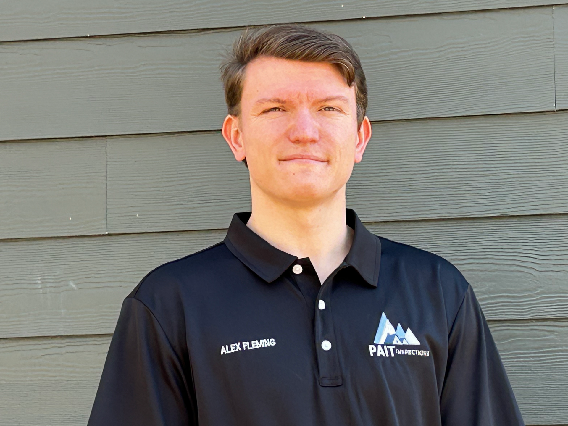 A man in a black shirt is smiling in front of a house.