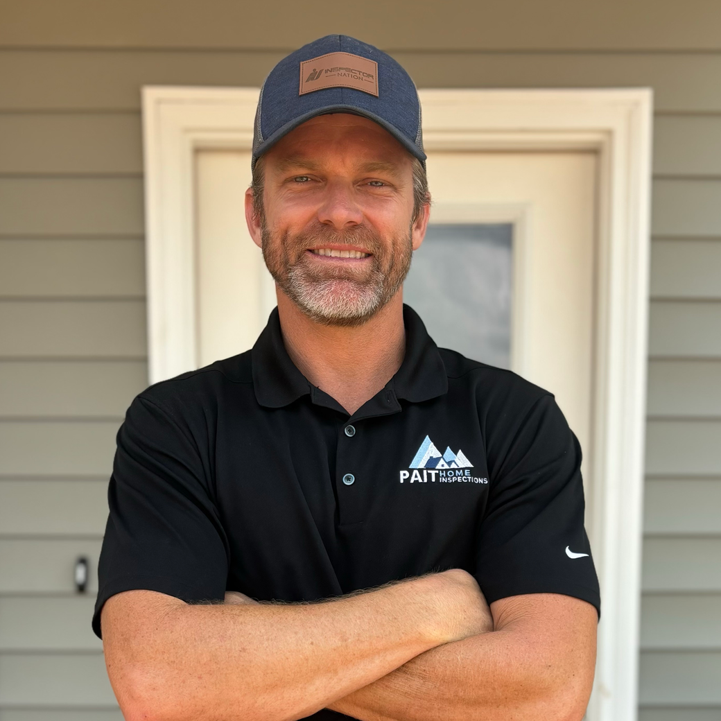 Stephen Pait wearing a black shirt and a blue hat is standing in front of a door with his arms crossed.