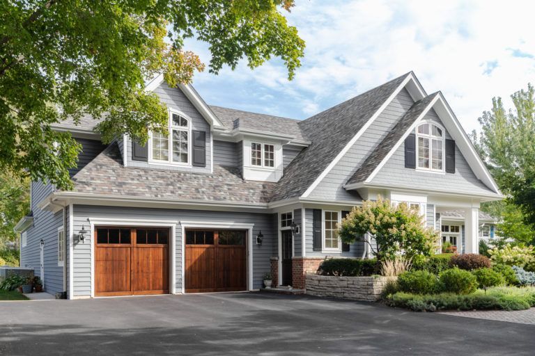 A large house with two garage doors is sitting on top of a lush green hillside.