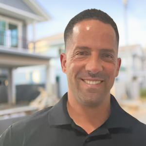 A man in a black shirt is smiling in front of a house.