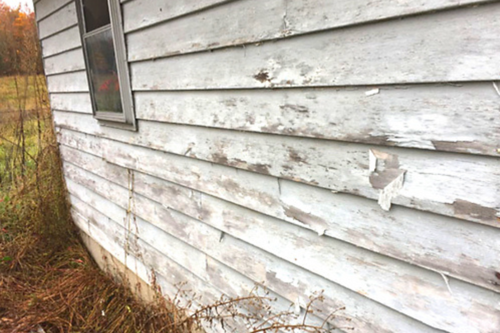 The side of an old white house with peeling paint and a window.