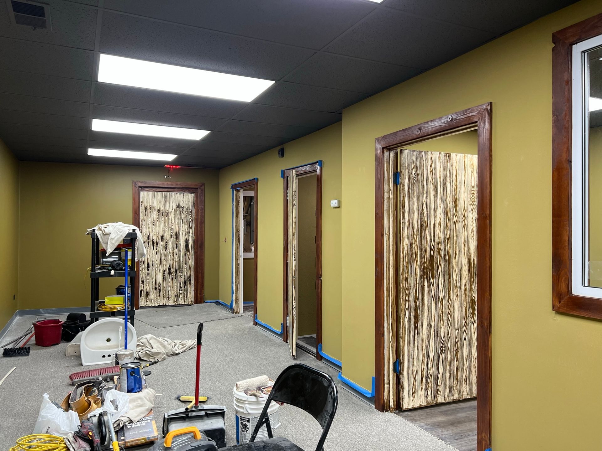 Hallway under renovation with mustard walls, dark ceiling, wooden door frames, and doors.