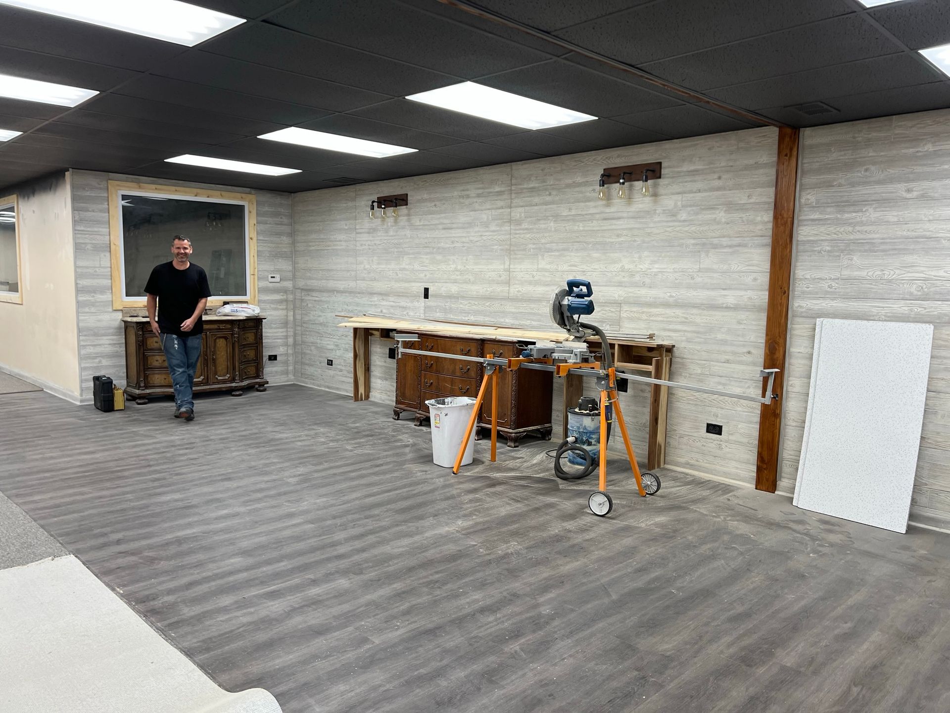 Man stands in unfinished room with exposed beams, workbench, and a saw.