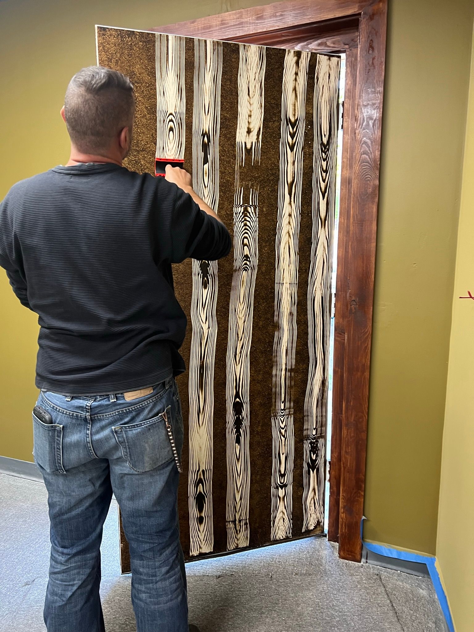 Man installing patterned door covering; brown, white and black vertical stripes on a dark wood doorframe.