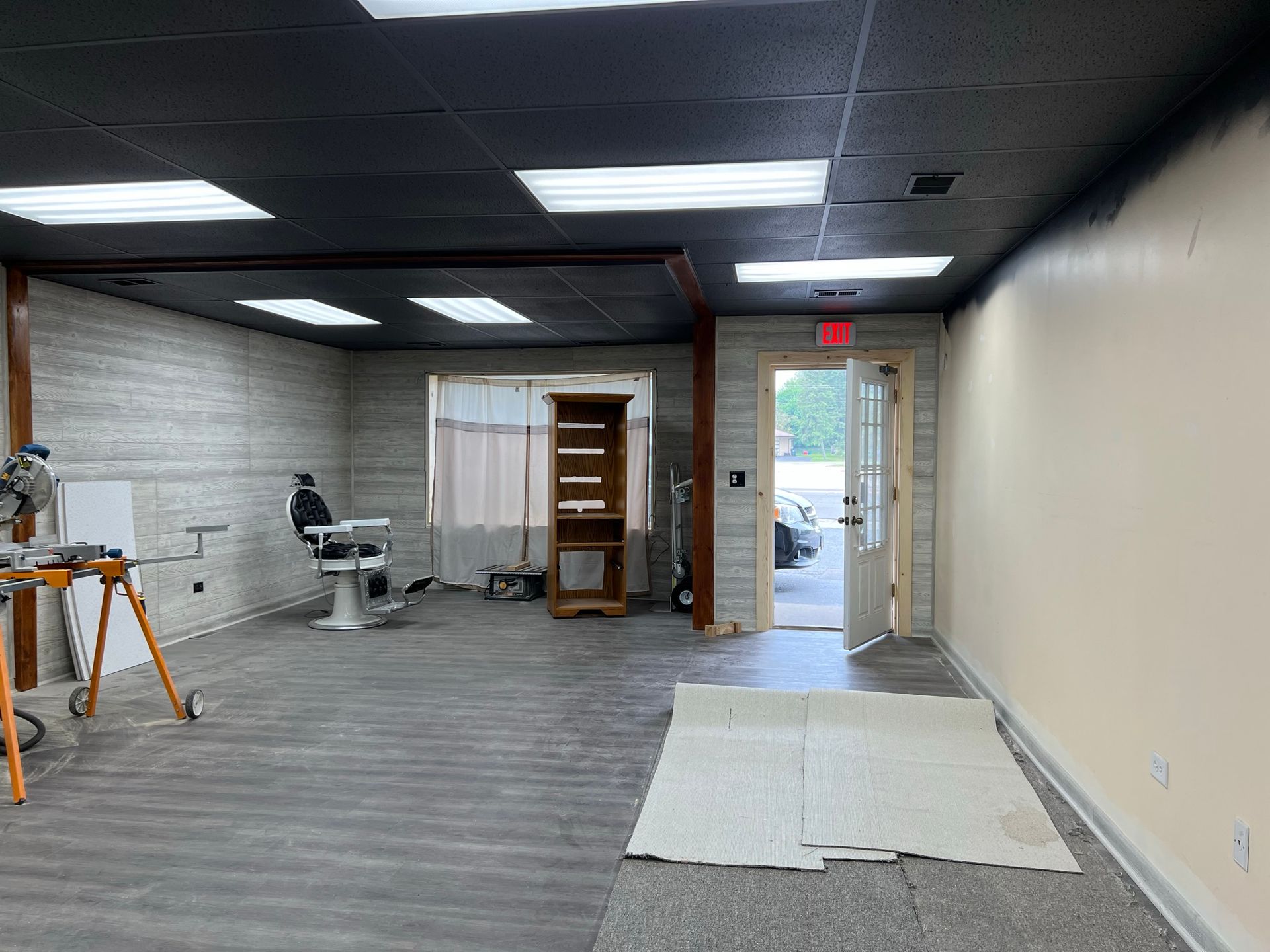 Interior of a room, partially renovated. Features gray flooring, a barber chair, and an open doorway.