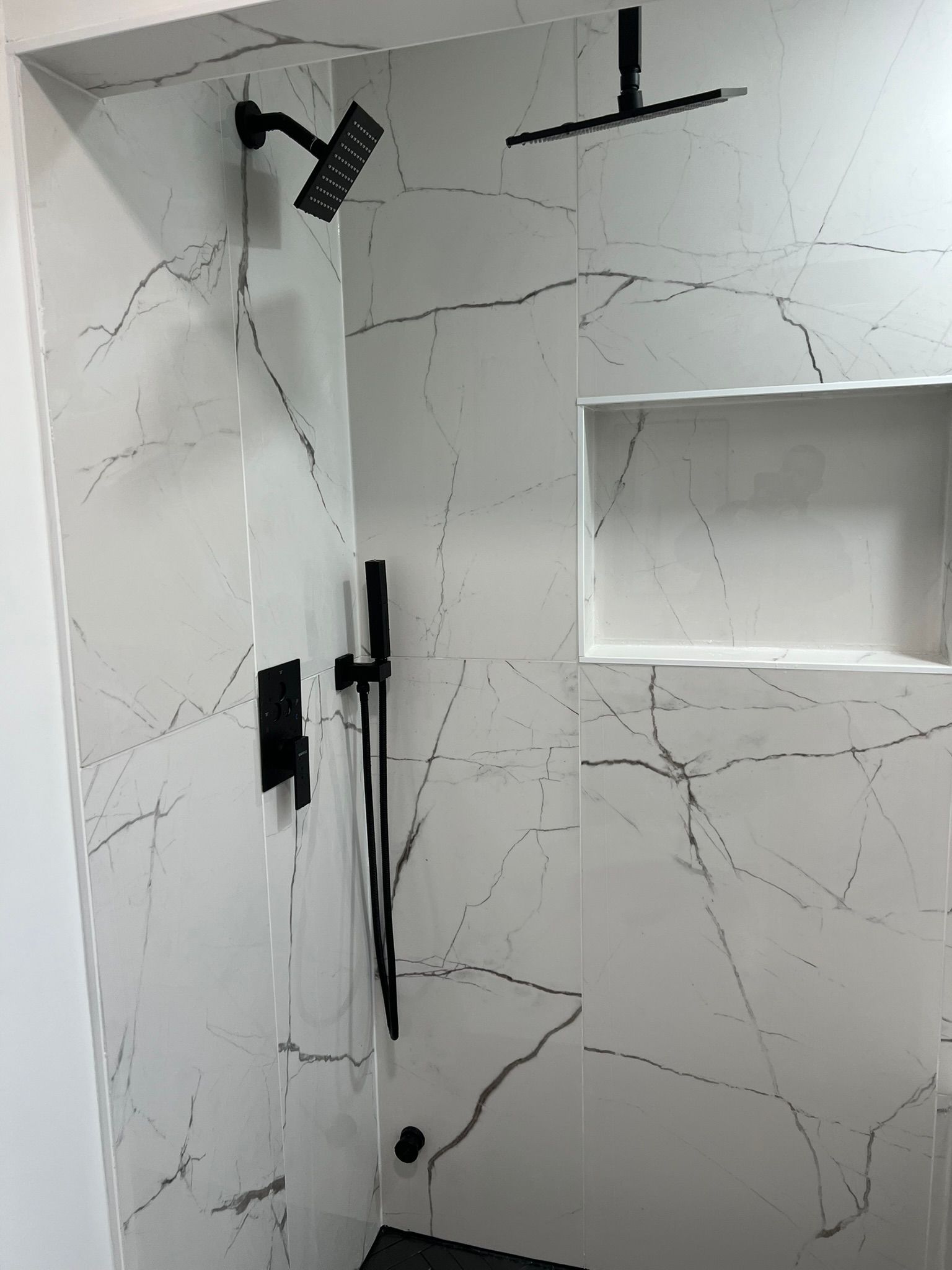 Black shower fixtures against white marble tile in a bathroom.