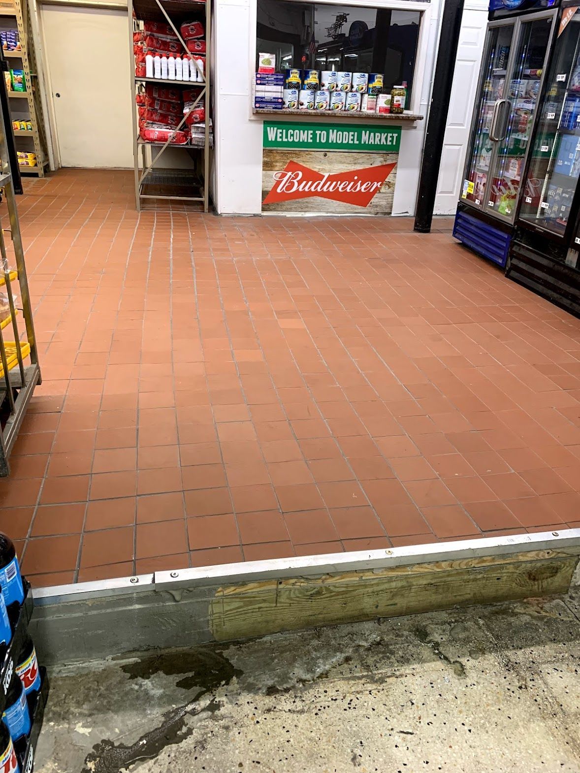 Interior of a market with red-tiled floor, a Budweiser sign, and various products for sale.