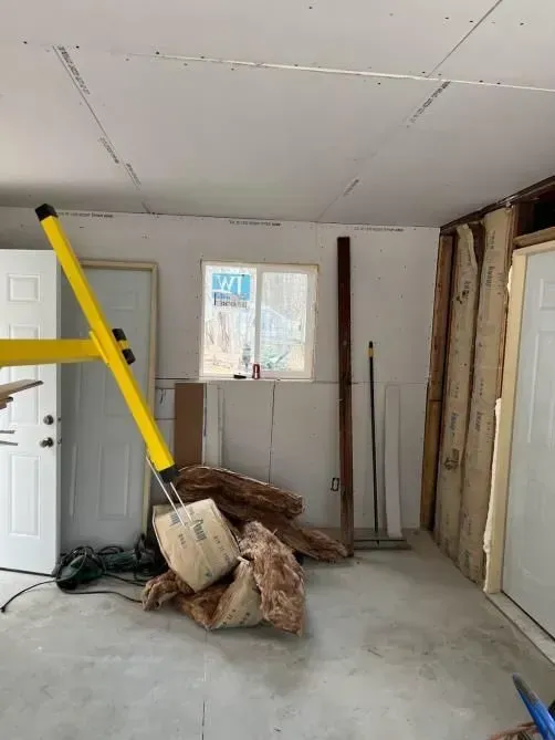 A room under construction; yellow ladder, debris, insulation, window, and doors.