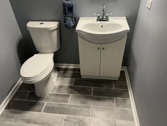 A small bathroom with a white toilet, sink, and gray tile floor. Blue walls.