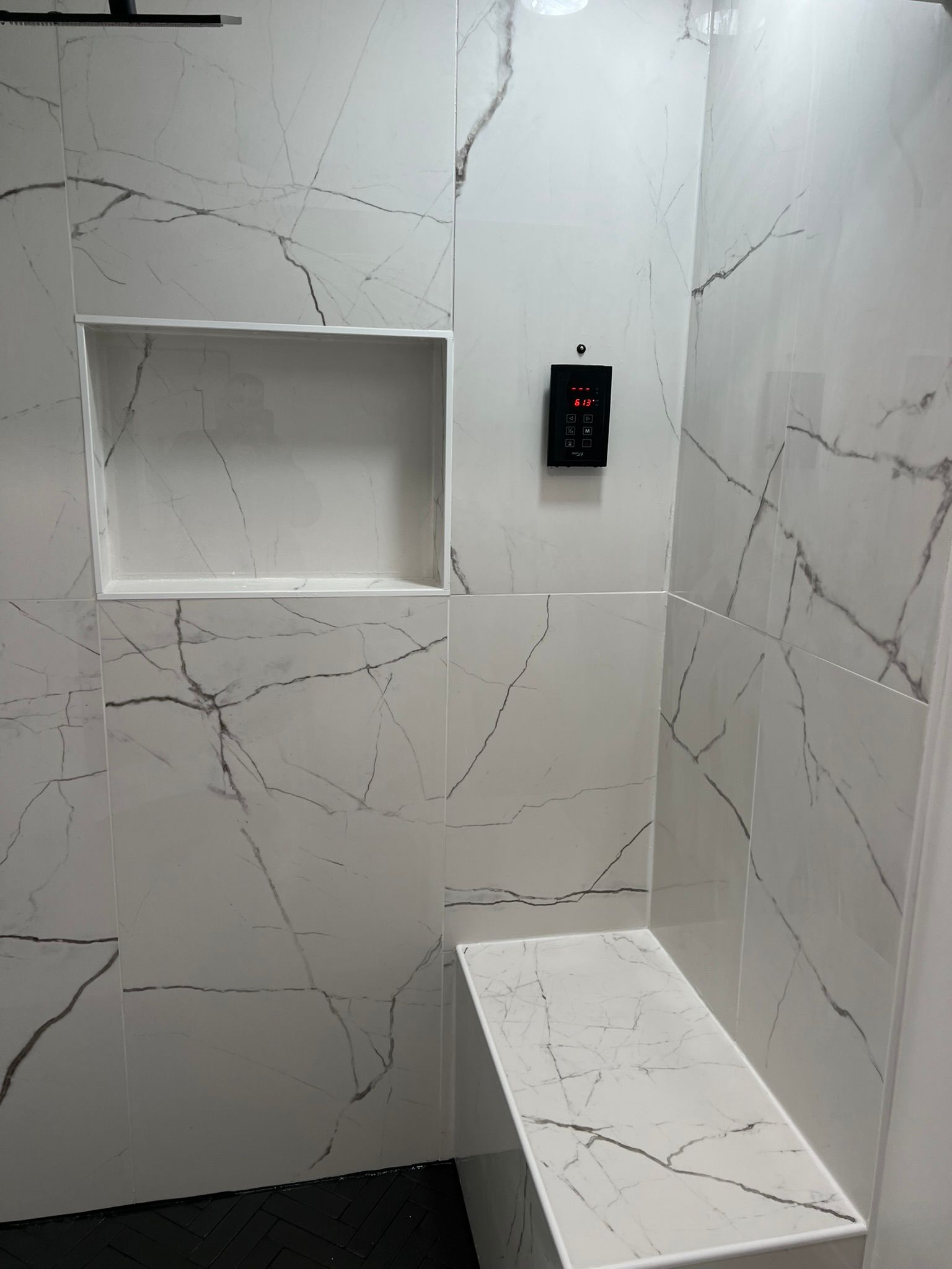 White and gray marble-tiled shower with a bench, a recessed shelf, and a control panel.