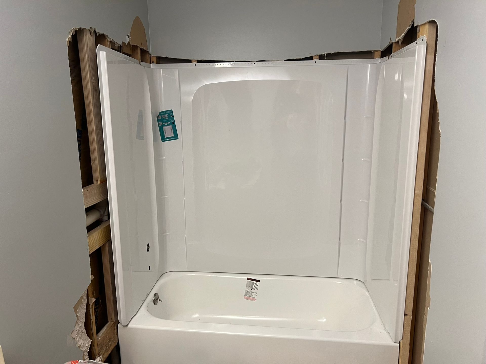 White bathtub and shower surround installed in a bathroom under construction, walls exposed.