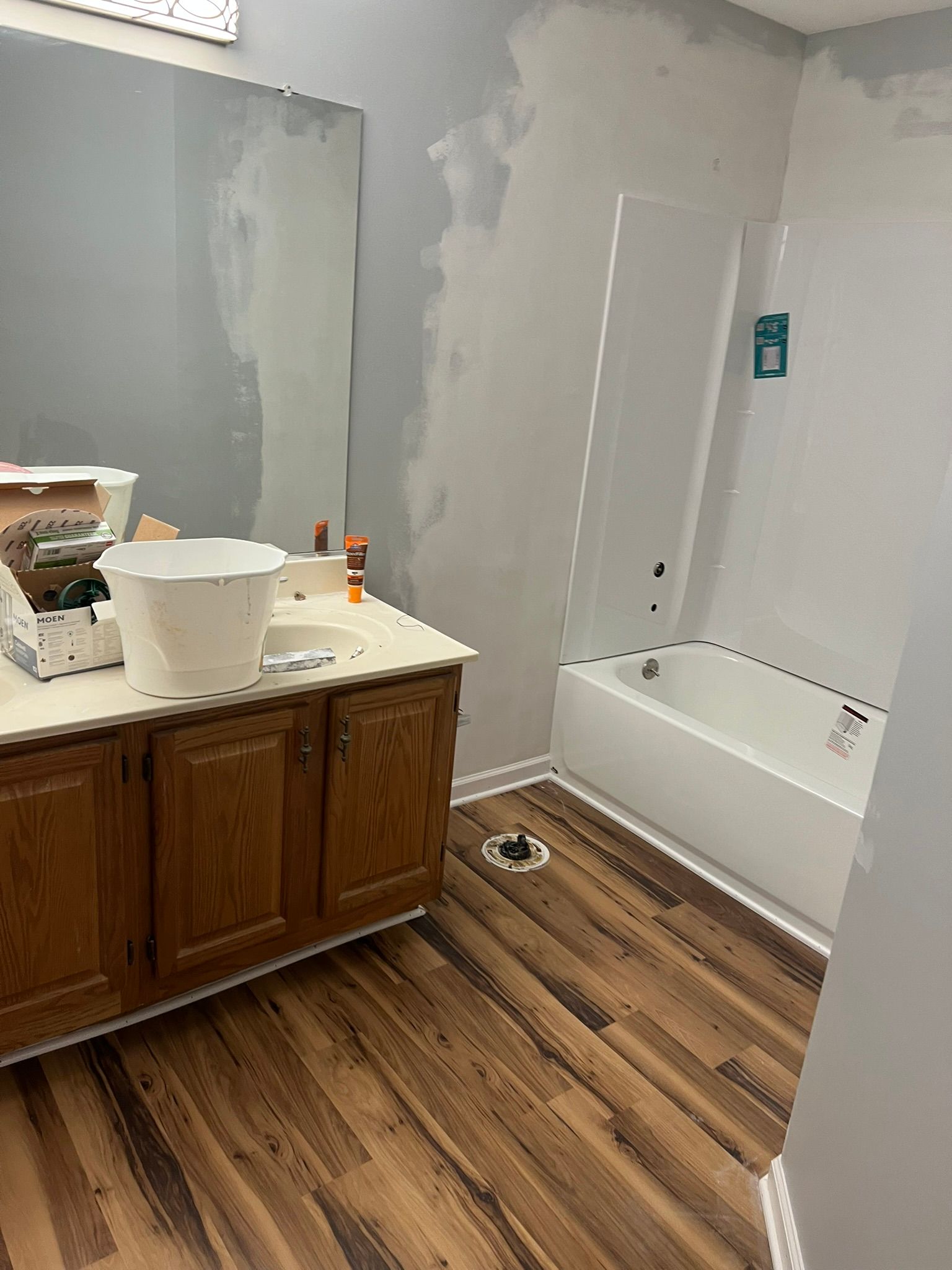 Bathroom with oak vanity, bathtub, and faux wood floor. Walls are partially painted light gray.