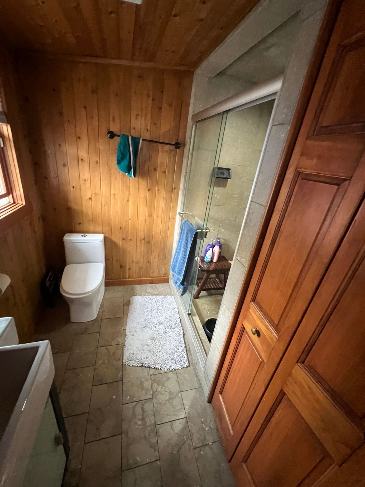 Bathroom with wooden paneling, toilet, shower, and large wooden cabinet.