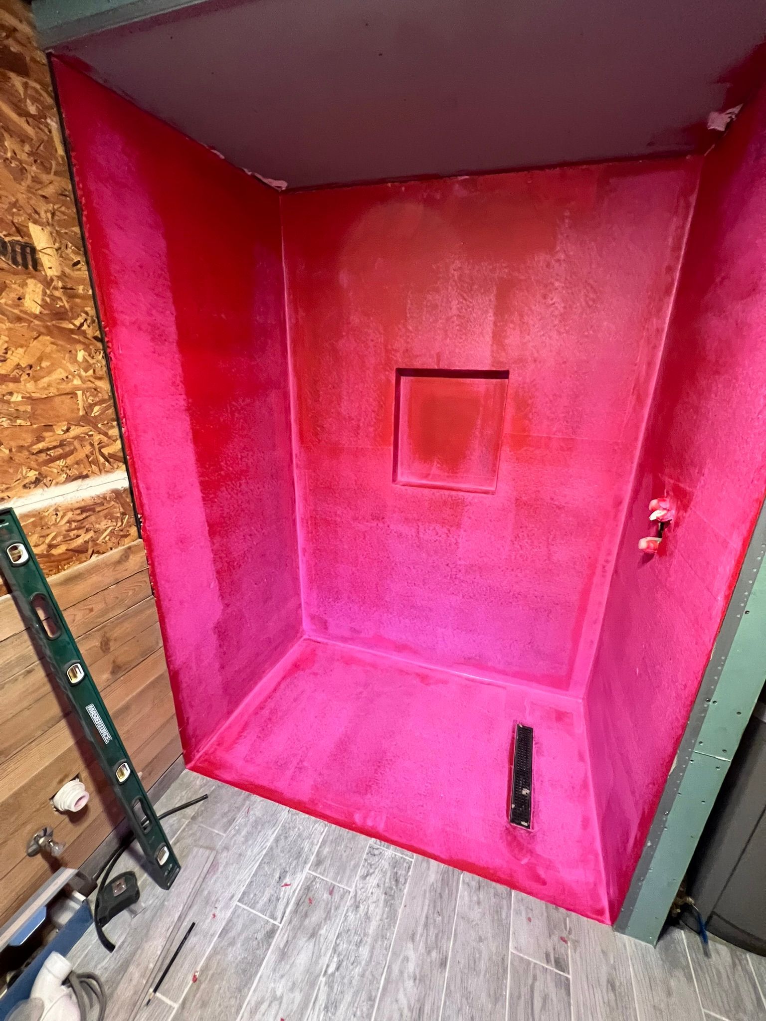 Pink shower stall under construction; gray floor, wooden walls, tools visible.