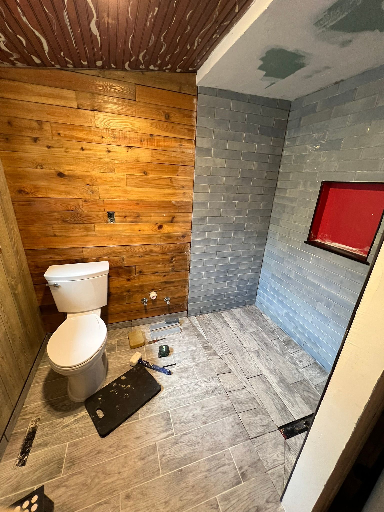 Bathroom renovation in progress with wood paneling, gray tile, and a toilet.