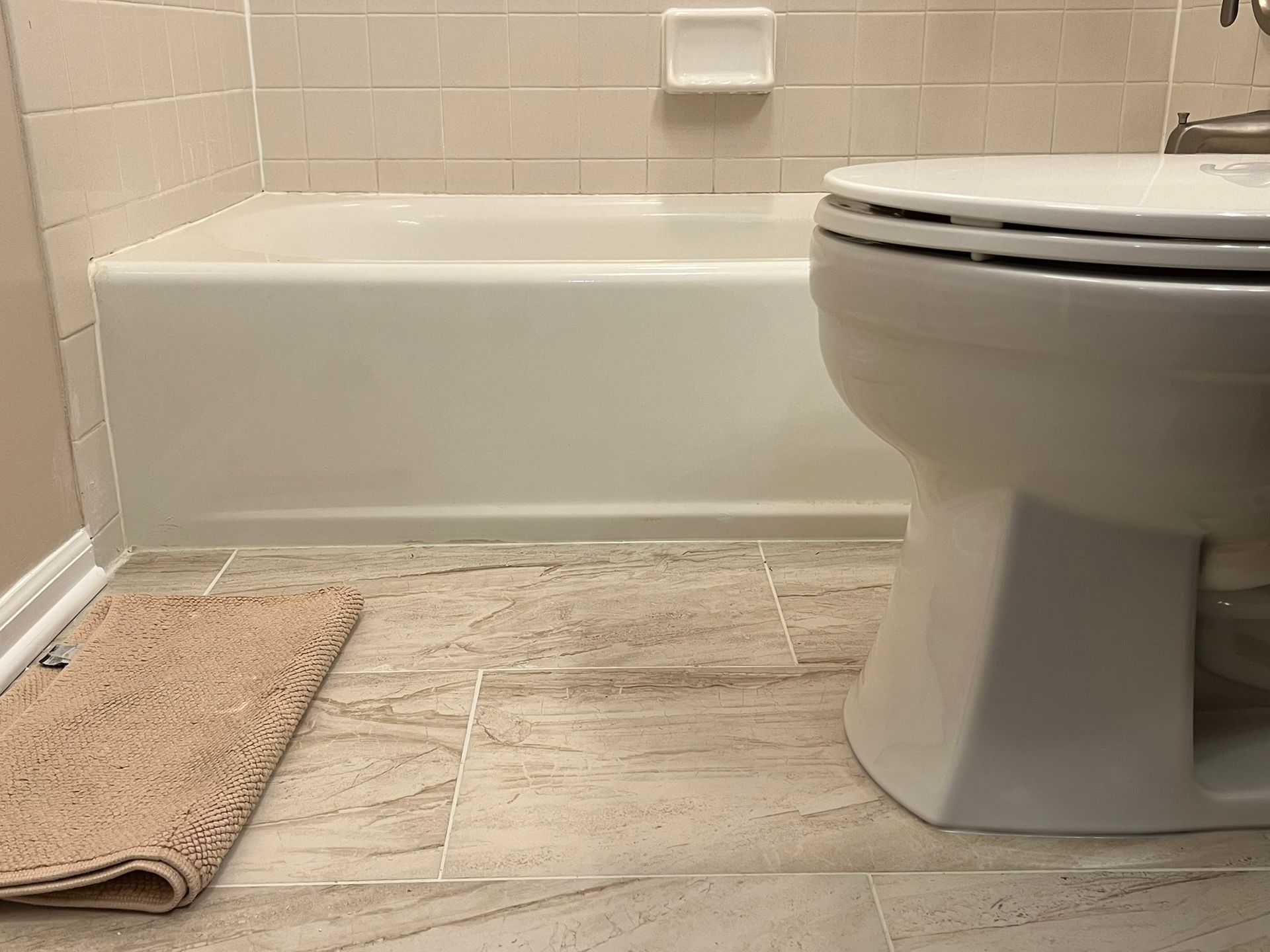 Bathroom with a white bathtub, toilet, and beige bath mat.