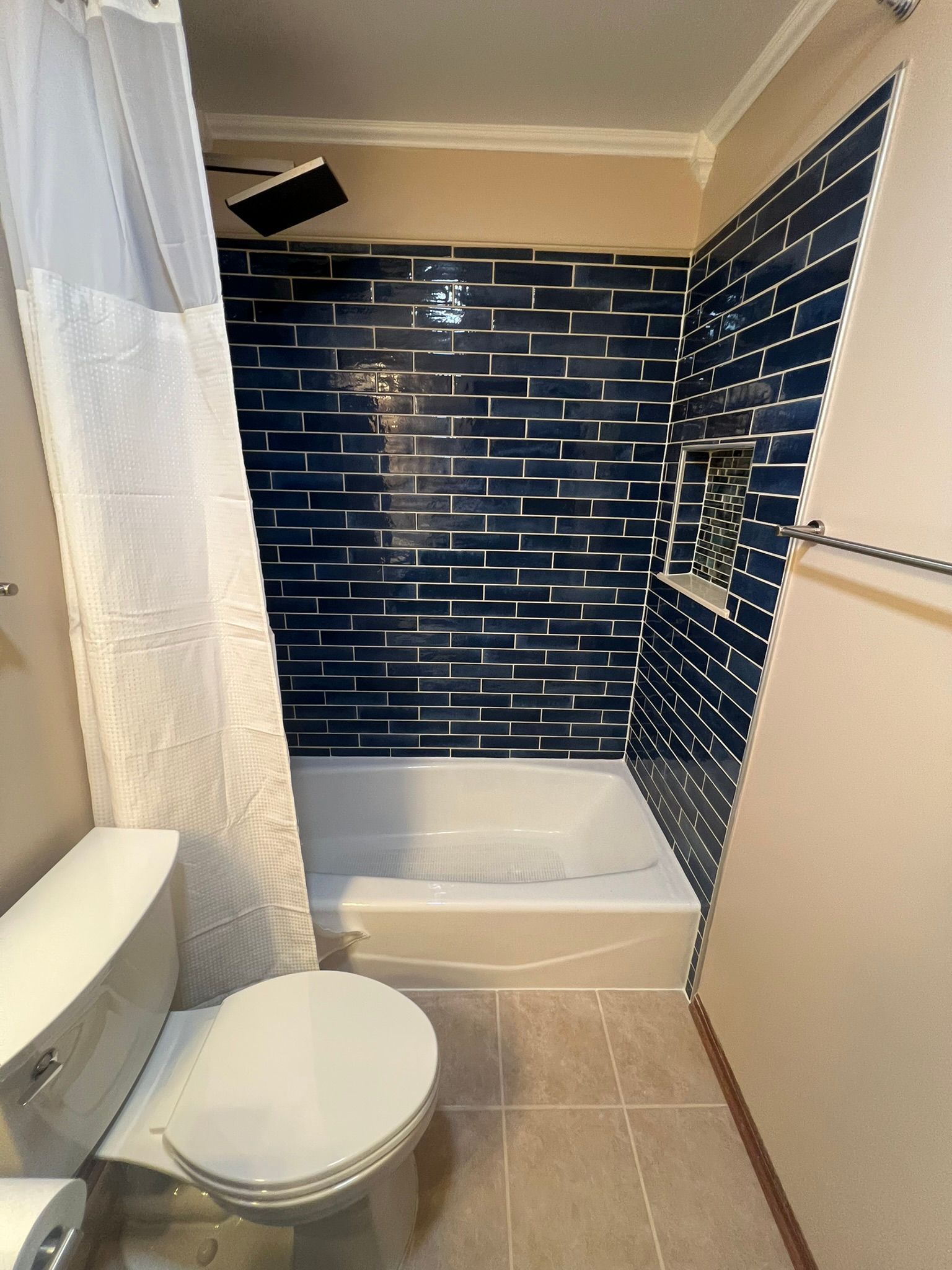 Bathroom with blue tiled shower, toilet, and beige floor.