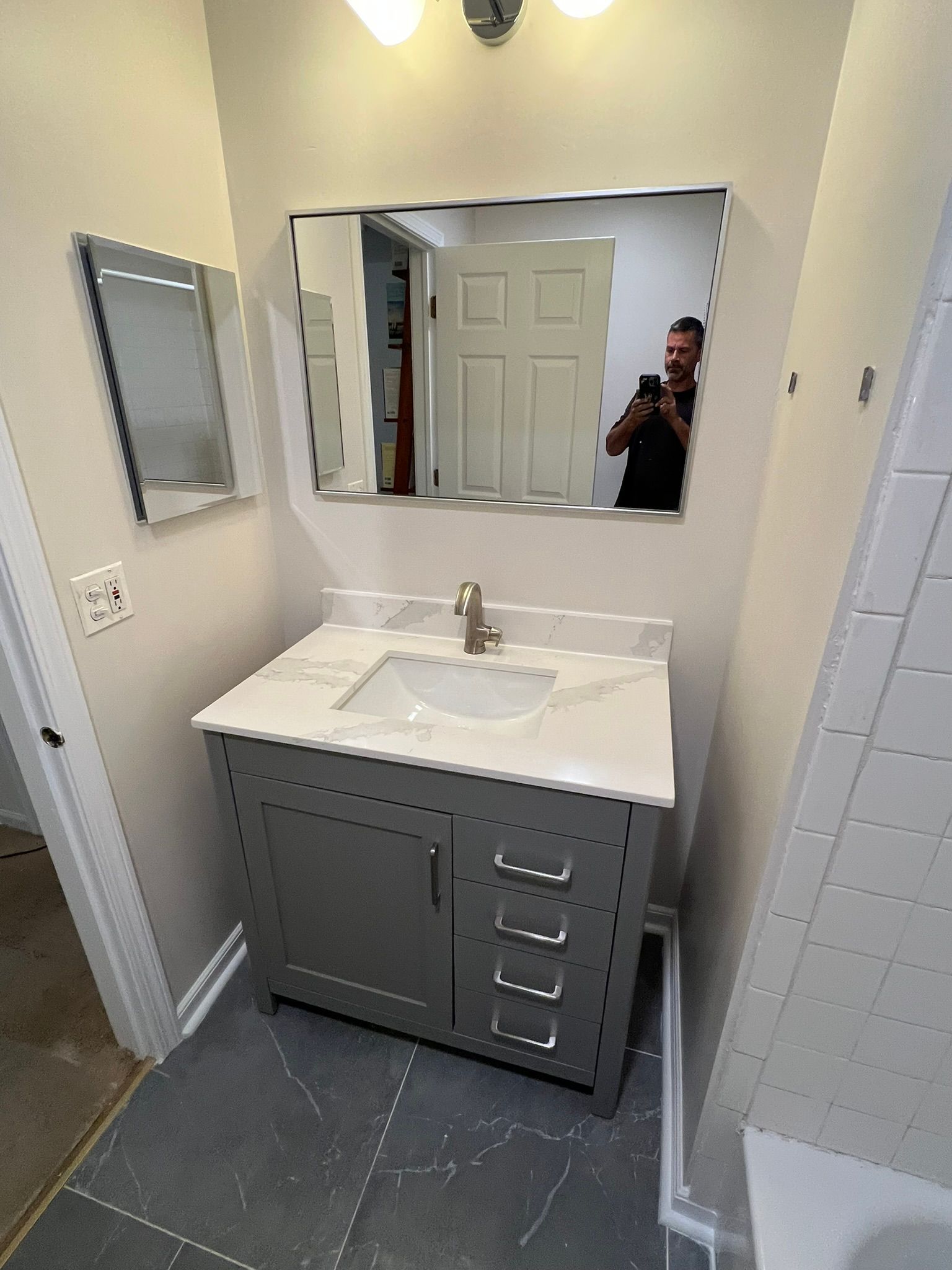 Bathroom with gray vanity, white countertop, large mirror, and gray floor tiles.
