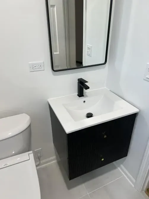 Black floating bathroom vanity with a white sink, faucet, and mirror. White toilet on the left.