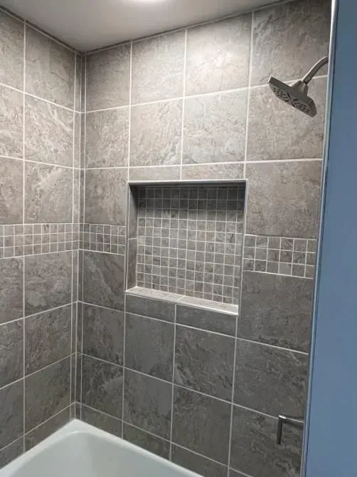 Gray tiled shower with a built-in niche and a decorative tile band; showerhead visible.
