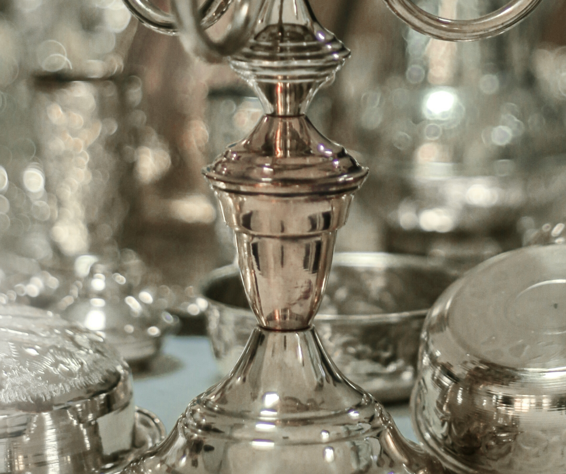Primo piano di un candelabro d'argento, circondato da altri oggetti d'argento, probabilmente in un negozio o in una vetrina.