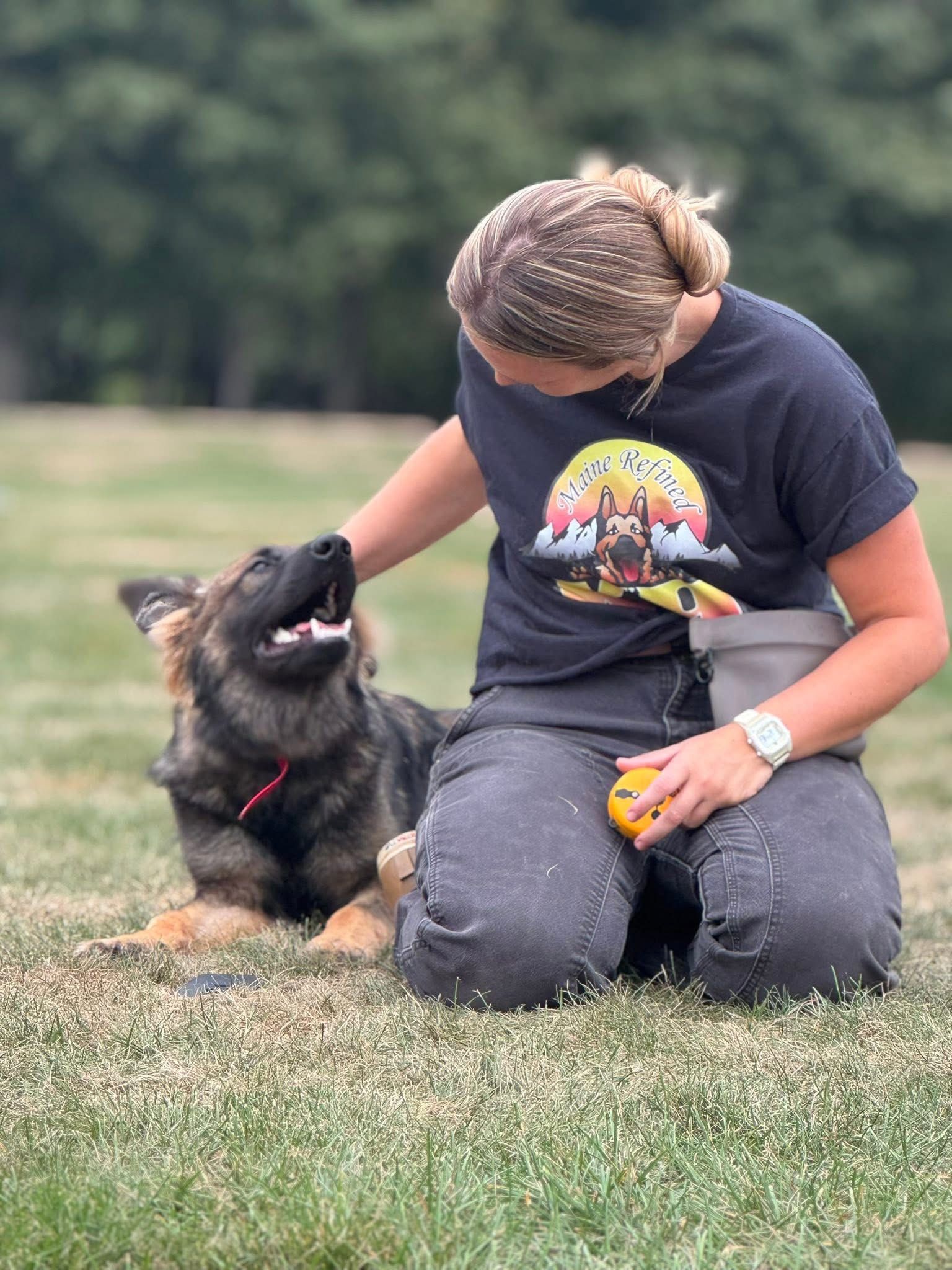 Woman kneels to pet a German Shepherd puppy outdoors. The puppy looks up with an open mouth.