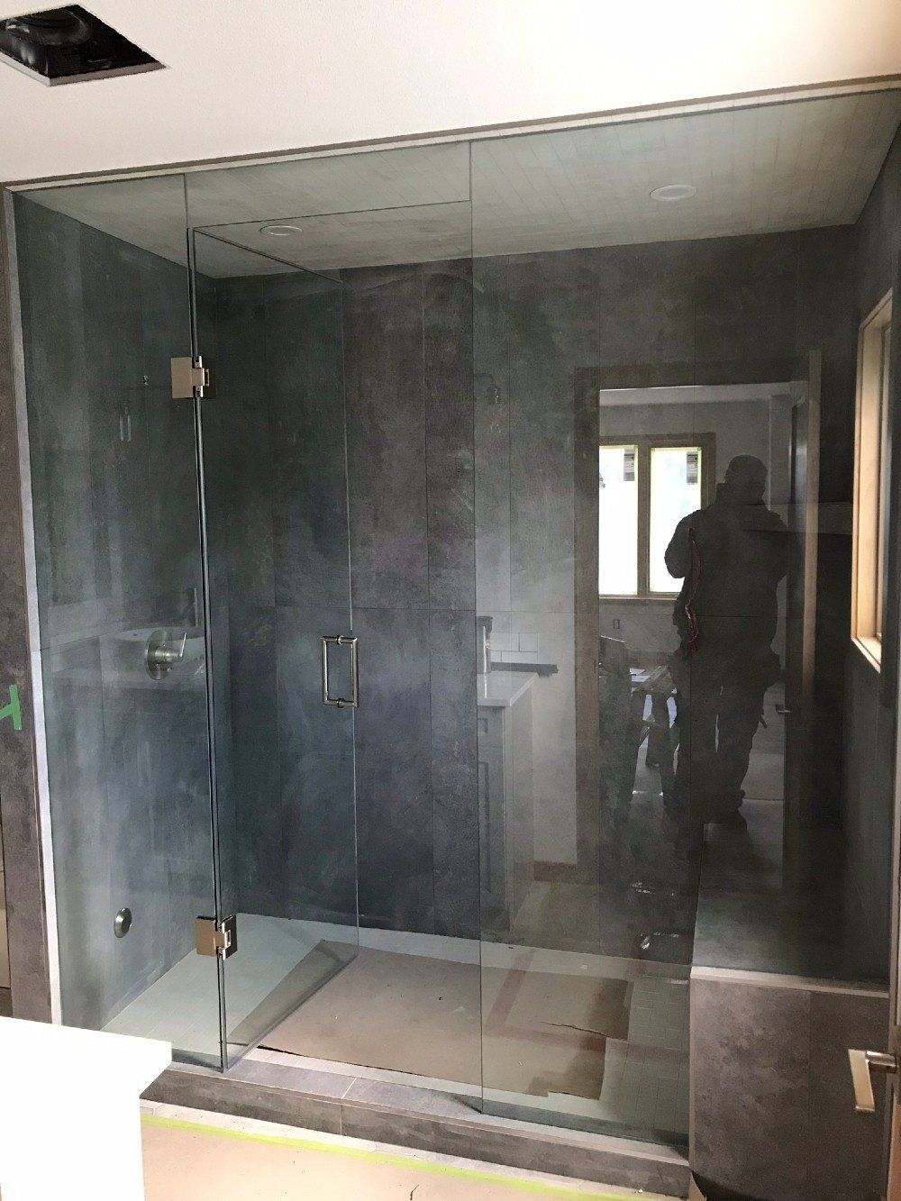 A man is standing in a bathroom with a glass shower door.