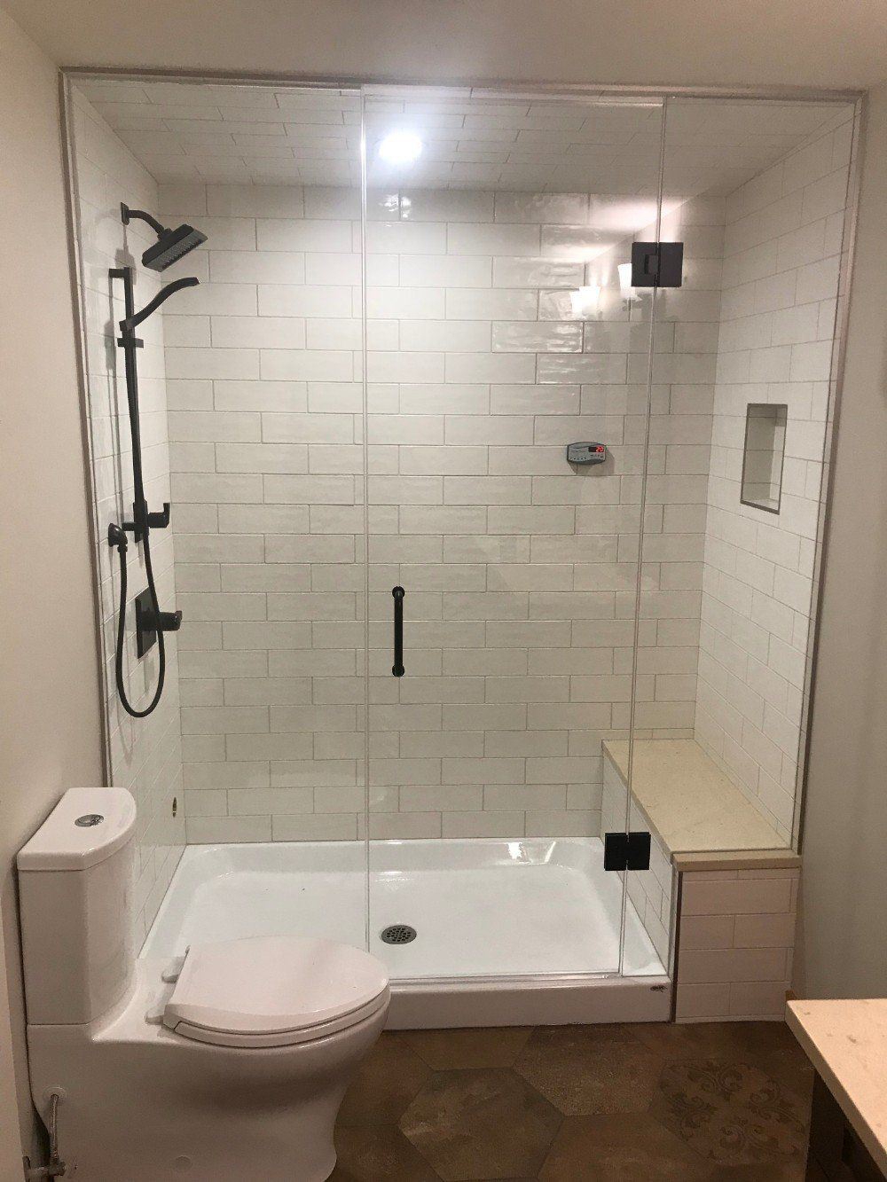 A bathroom with a toilet , shower , and glass door.
