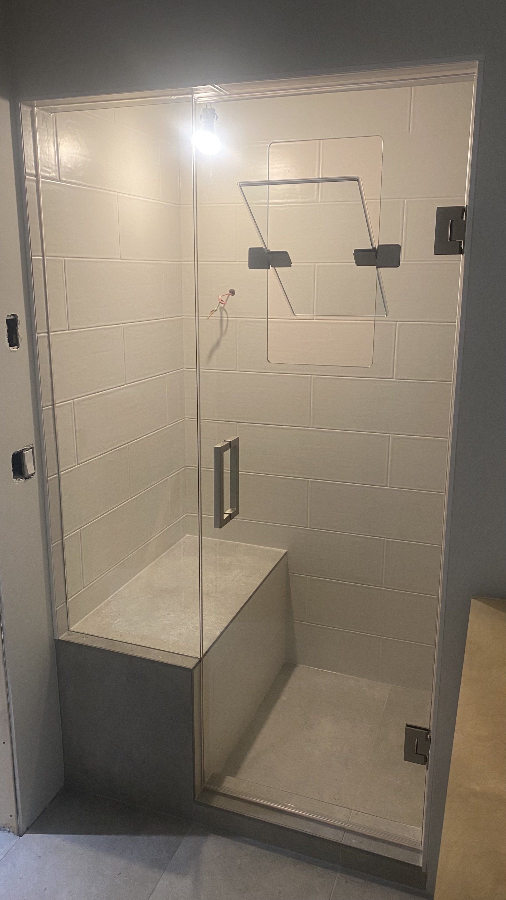 A shower with a bench and a glass door in a bathroom.